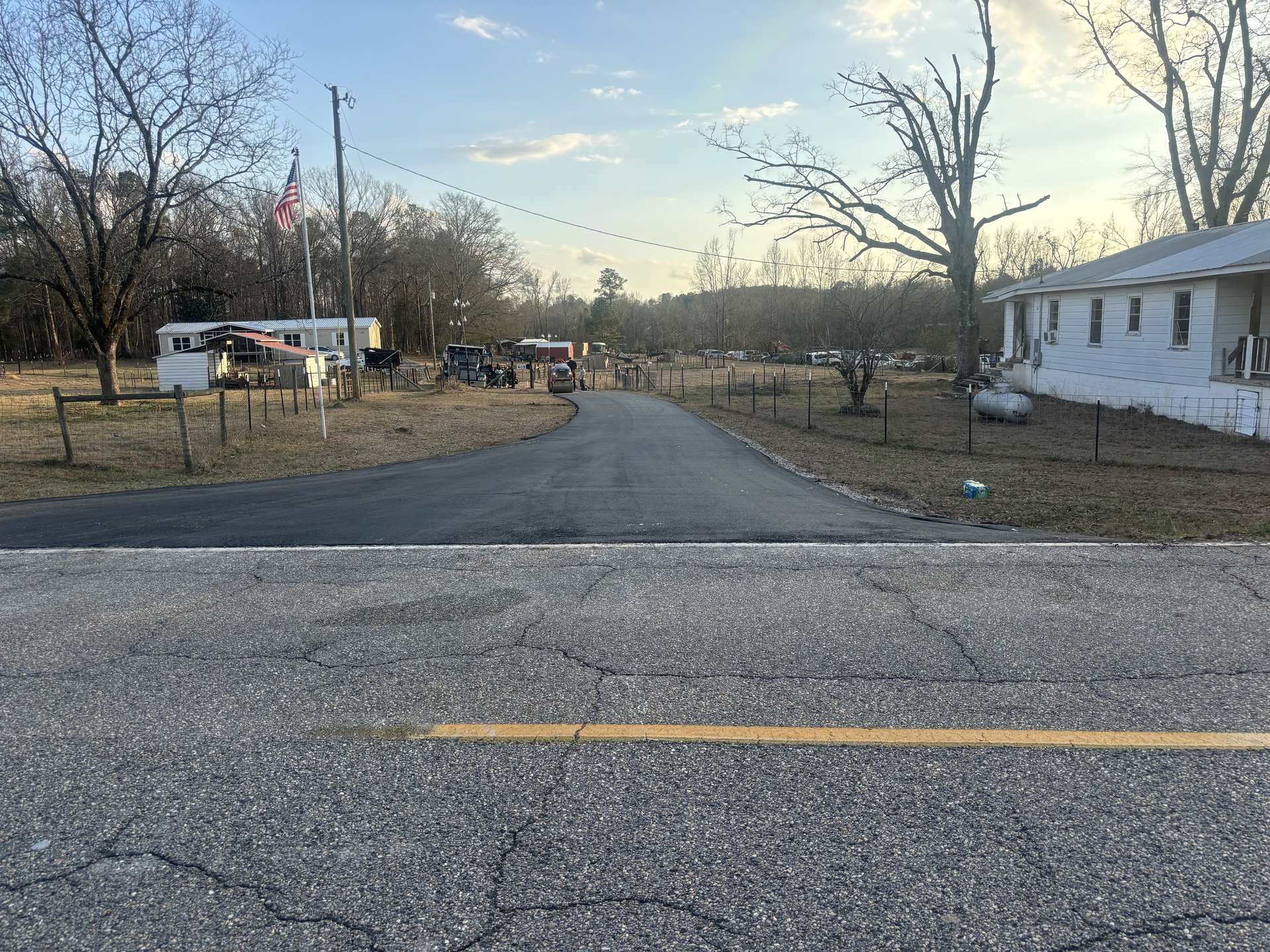 A freshly paved country road running past homes and fields
