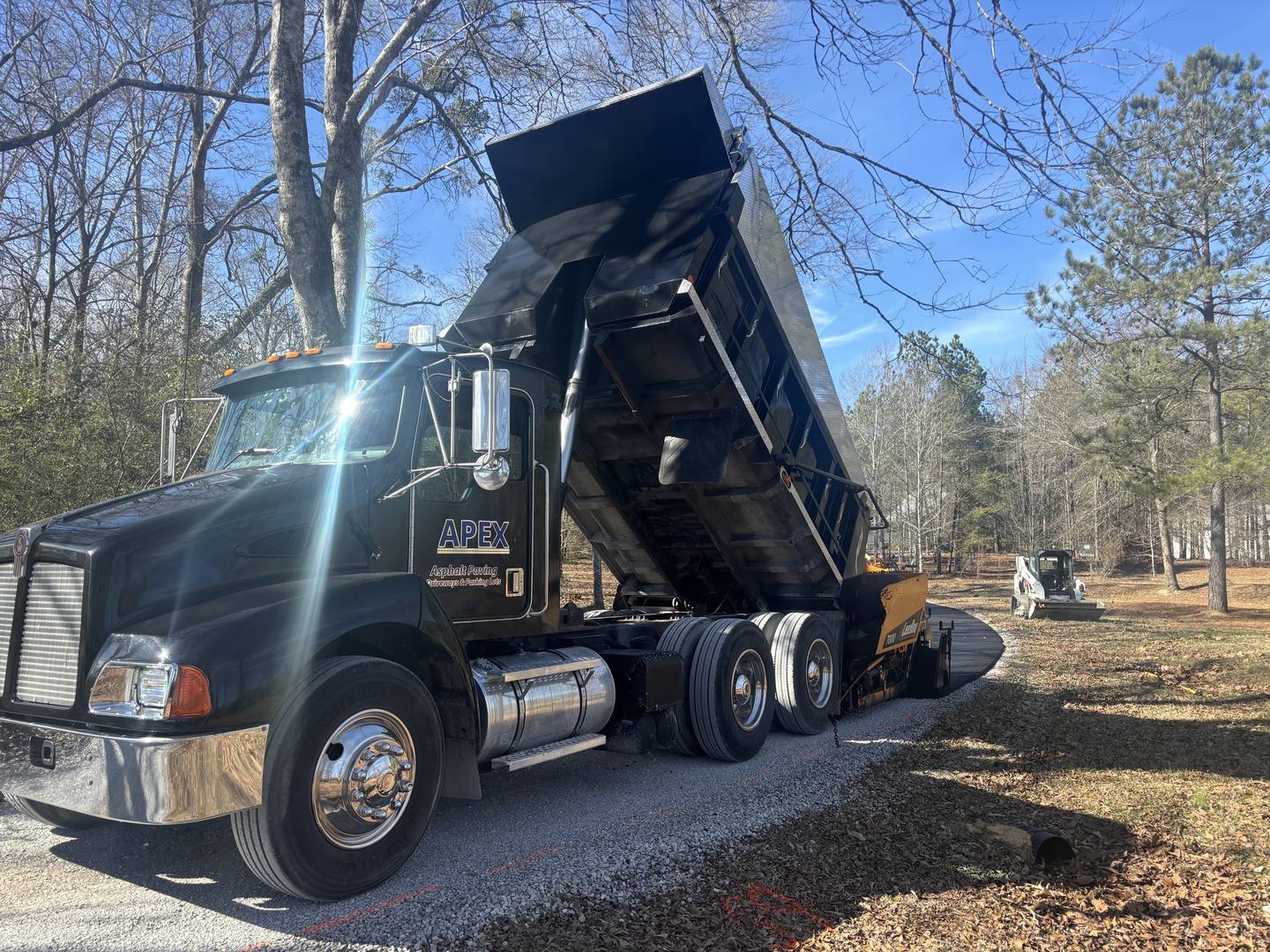 An Apex dump truck raising its bed beside a gravel drive